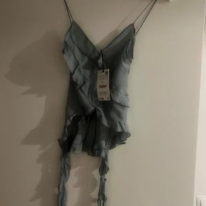 Ljusblå topp från Zara - Säljer en elegant ljusblå topp från Zara med smala axelband och volangdetaljer. Oanvänd 