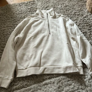 Beige tröja med dragkedja från 157 - Säljer en stilren beige tröja från 157 med halv dragkedja och hög krage. Perfekt för en avslappnad look. Tröjan har långa ärmar och ribbade muddar vid ärmslut och nederkant.