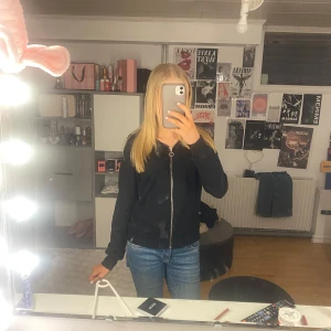 Svart bomberjacka med dragkedja - Säljer en stilren svart bomberjacka med dragkedja framtill. Jackan har långa ärmar och en klassisk passform som passar perfekt till vardags. Enkelt att matcha med olika outfits.