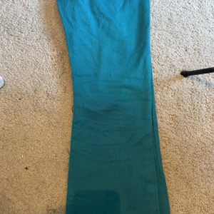 Turkosa byxor från Trend - Snygga turkosa byxor från Trend med en utsvängd passform . Byxorna har en stilren design med en knappdetalj framtill. Perfekta för att lägga till en färgklick i garderoben!