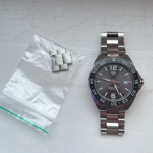 TAG Heuer Formula 1 Date - Snygg TAG Heuer Formula 1 klocka med automatisk urverk och datumvisning. Den har en stilren svart urtavla med vita och röda detaljer samt en robust boett i stål. Armbandet är också i stål och klockan är vattentät upp till 200 meter. Perfekt för den som gillar sportig elegans. Klockan är otroligt bra skick med några få repor. Test paper och äkthets bevis finns även en klockbox men inte orginalet eftersom jag har tappat bort den, fick denna I konfirmations present och nypris är 30000kr.
