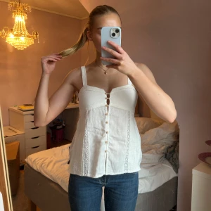 Vit ärmlös topp från Zara - Säljer en vit topp från Zara med fina knappar framtill. Toppen har fina spetsdetaljer och en lätt ribbad struktur på sidorna. Aldrig använd och prislappen sitter kvar💖