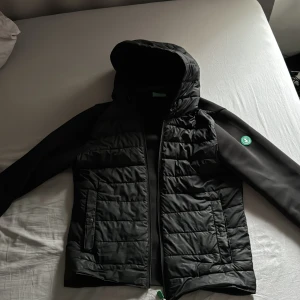 Svart jacka från Save the Duck - Snygg svart jacka från Save the Duck med huva. Jackan har en quiltad design på framsidan och ett grönt märke på ärmen. Perfekt för kyligare dagar med sin moderna look och funktionella detaljer bara höra av er vid funderingar 👍, pris går såklart o diskutera 