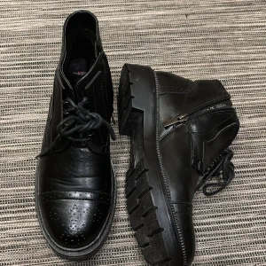 Svarta boots med snörning och dragkedja - Snygga svarta boots i skinn med både snörning och dragkedja på sidan. Skorna har en robust sula och dekorativa perforeringar på tån. Perfekta för en stilren look.