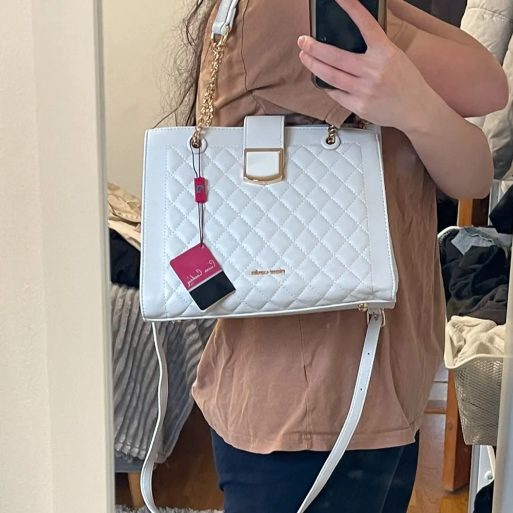 Snygg vit handväska från Pierre Cardin med quiltat mönster och guldfärgade kedjedetaljer. Väskan har en elegant spänne framtill och justerbar axelrem. Perfekt för att ge din outfit en lyxig touch.. Laukut & Käsilaukut.