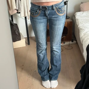 Blåa bootcut jeans med låg midja - Trendiga lågmidjade jeans. Några stenar saknas från bakfickorna och de har ett litet hål under en av skärpöglorna (bild 5 i övre höger hörn) men annars ska det inte vara några andra defekter.
