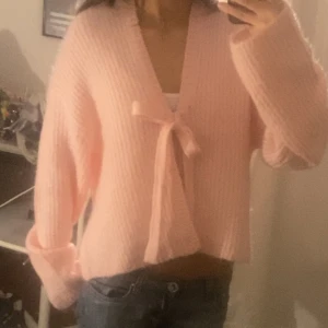 Rosa stickad kofta med knytband - Säljer en söt rosa stickad kofta med knytband framtill. Koftan har långa ärmar och en mjuk, ribbad textur som ger en mysig känsla. Perfekt för att lägga till en feminin touch till din outfit. Passar bra till jeans eller kjol. Säljer pga den inte har kommit till användning, endast använd för att ta bild och i provrummet💗 Går att styla på många sätt, passar från storlekar XS-L
