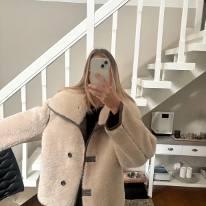 Beige teddyjacka med knappar - Mysig beige jacka  med stora knappar och kontrasterande mörka detaljer. Jackan har en bred krage och långa ärmar, perfekt för kyliga dagar. Den har en loose passform som ger en avslappnad stil. Använt 1 gånger så i nyskick ☺️