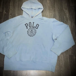 Ljusblå hoodie från Polo Ralph Lauren - Säljer en ljusblå hoodie från Polo Ralph Lauren med stor logga på framsidan. Tröjan har en klassisk känguruficka och en bekväm huva. Perfekt för en avslappnad stil.
