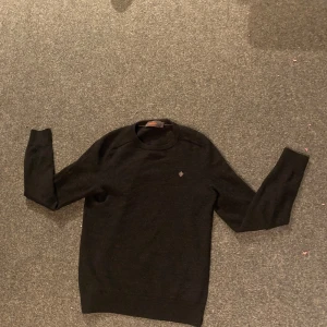 Svart stickad tröja från Morris - Säljer en stilren svart tröja från Morris med ett diskret broderat emblem på bröstet. Tröjan har långa ärmar och en klassisk rund halsringning. Perfekt för en elegant och avslappnad look. Tröjan är S men sitter som XS