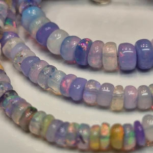 Färgglatt halsband med opalpärlor - Säljer ett vackert halsband med skimrande opalpärlor i olika nyanser av lila, blått och rosa. Halsbandet har en justerbar kedja i silverfärg och ett smidigt lås. Perfekt för att ge en färgglad touch till din outfit.