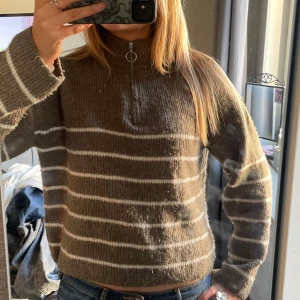 Brun randig tröja från Vero Moda - Säljer en mysig brun tröja från Vero Moda med vita ränder. Tröjan har en dragkedja vid halsen och långa ärmar!