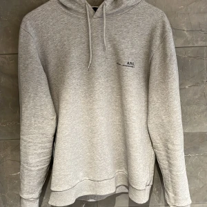 A.P.C Hoddie - Säljer en stilren grå hoodie från A.P.C. med tryck på bröstet. Tröjan har en klassisk design med huva och dragsko samt ribbade muddar. Perfekt för en avslappnad look. Skick 9,5/10 nästan helt ny. Nypriset ligger runt 2500kr.
