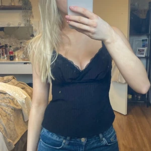 Svart ribbad topp - Snygg svart ribbad linnetopp med spetsdetaljer vid urringningen. Perfekt för en stilren look och kan enkelt matchas med jeans eller kjol.