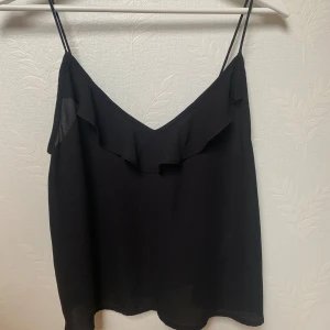 Svart volang linnetopp - Säljer en svart linnetopp från Gina Tricot, stl XS 💕Toppen har tunna axelband och en söt volangdetalj framtill. Nästan aldrig använd så är i jättebra skick!