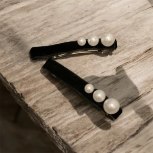 Svarta hårklämmor med pärlor - Två eleganta svarta hårklämmor dekorerade med vita pärlor i olika storlekar. Perfekta för att ge en stilfull touch till din frisyr. 35 kr för ett par 