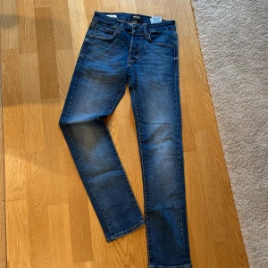 Blå jeansbyxor J&J 27/30 - Snygga blå jeansbyxor med klassisk femficksdesign och knappgylf. De har en smal passform och är perfekta för en avslappnad stil. Midjemåttet är 27 och längden 30, vilket ger en bra passform för många.