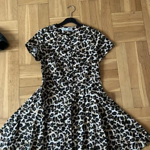 Leopardmönstrad klänning från Zara - Snygg leopardmönstrad klänning från Zara med korta ärmar och knappar framtill. Perfekt för att sticka ut med ett djärvt mönster. Klänningen har en flödande passform som ger en bekväm känsla.