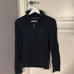 Mörkblå tröja från Tommy Hilfiger - Säljer en stilren mörkblå tröja från Tommy Hilfiger i premium bomull. Tröjan har en dragkedja vid halsen och ett litet logotypmärke på bröstet. Perfekt för en avslappnad och snygg look. Säljer denna då jag växt ur den. Ställ frågor vid minsta funderingar