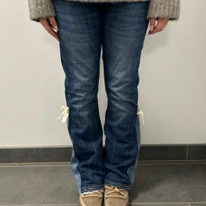 Blå jeans med rosett och spetsdetalj - Snygga blå jeans med unika detaljer som rosetter på sidorna och spets vid bensluten. Perfekta för dig som vill ha något extra i garderoben. Jeansen har en klassisk passform och är tillverkade i ett bekvämt denimtyg.