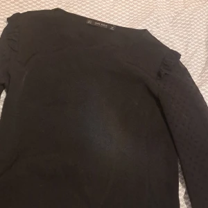Svart tröja från Zara Basic - Snygg svart tröja från Zara Basic med prickigt mönster på ärmarna och volangdetaljer vid axlarna.Tröjan har en normal passform och är tillverkad i ett mjukt material✨.