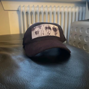 Svart keps från Emilio Pendenza - Snygg svart keps från Emilio Pendenza med ett unikt tryck framtill. Kepsen har justerbar passform med ett spänne baktill för optimal komfort. Perfekt för en cool och avslappnad stil.