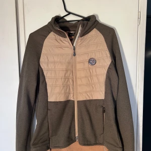 Beige och brun jacka från JH Collection - Säljer en snygg beige och brun jacka från JH Collection. Jackan har en dragkedja. Den är långärmad och har ett märke på bröstet. Perfekt för kyligare dagar!