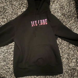 Svart hoodie med Ice Cube-tryck - Cool svart hoodie med rosa text 'ICE CUBE' på framsidan och 'TODAY WAS A GOOD DAY' längs ärmarna. Baksidan har ett stort tryck av Ice Cube i grått och rosa. Perfekt för fans av hiphop och streetwear.✨💫💫