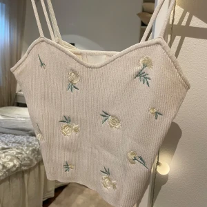 Beige ribbad linnetopp med blommor - Säljer detta linne/ tubtop men små söta blommor på. Säljer då ja inte använder den💕