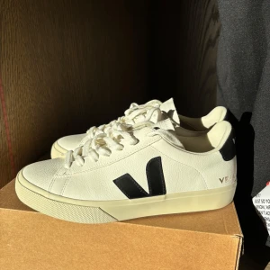 Vita sneakers från Veja - Snygga vita sneakers från Veja med svarta detaljer och snörning. Skorna har märkets logga på sidan och hälen. Köpte för 1695 och är oanvända