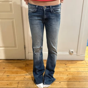 Lågmidjade Lee jeans - Lågmidjade jeans från Lee med hål, passar XS/S. Midja 37cm, innerbenslängd 84cm