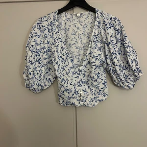  blommig blus från H&M - Säljer en söt vit blus från H&M med blått blommönster. Köpt förra sommare och är knappt använd.