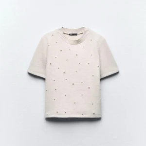 Topp med pärlor från Zara - Säljer en stilren tröja från Zara med korta ärmar och dekorativa pärlor över hela framsidan. Perfekt för en elegant look. Tröjan har en ribbad rund halsringning.
