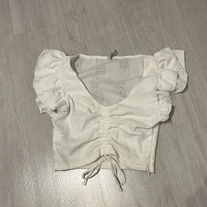 Vit blus med volangärmar - Charmig vit blus med korta volangärmar och knytning framtill. Blusen har en v-ringad design och är perfekt för sommarens varma dagar.