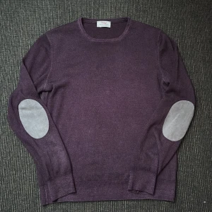 Lila tröja från Gran Sasso - Säljer en stilren kashmir, lila tröja i storlek m från Gran Sasso med rund hals och kontrasterande armbågslappar i grått. Perfekt för en elegant outfit! Tillverkad i Italien.