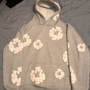 Grå denim tears hoodie - Säljer en grå denim tears hoodie med ett unikt blommönster i vitt. Tröjan har en klassisk känguruficka och en bekväm huva. Perfekt för en avslappnad stil. Skriv om ni har några frågor eller funderingar kring hoodien!😊