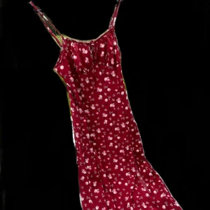 Röd blommig klänning - Charmig röd klänning med ett sött blommönster. Klänningen har smala axelband och en luftig passform som passar perfekt för varma dagar. Den är tillverkad i ett lätt och bekvämt material. Inte stretchig.