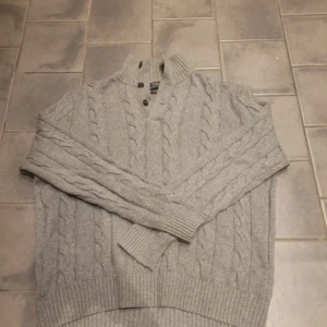 Grå kabelstickad tröja från Polo Ralph Lauren - Säljer en stilren grå kabelstickad tröja från Polo Ralph Lauren. Tröjan har en hög krage med knappar och ribbade muddar. 9/10 skick.  Perfekt för kyliga dagar. 🧶