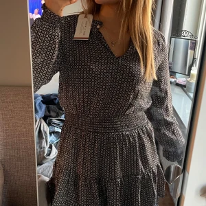 Mönstrad klänning  - Säljer en snygg mönstrad klänning från Lindex i svart och vit. Klänningen har långa ärmar, volang och stretchig vid midjan! Super fin till alla tillfällen. Stretchig så passar alla storlekar
