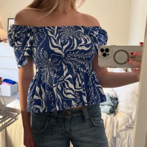 Volangtopp - En blå volang topp med vita detaljer. man kan både ha den som en offshoulder topp eller vanligt. Köpt från H&M, storlek M men passar en S. Aldrig använd. 