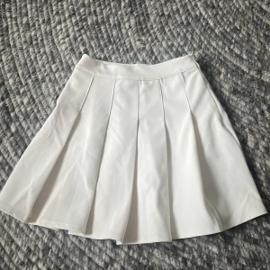 Vit kjol från FB Sister - Säljer en superfin vit kjol från FB Sister i storlek XXS. Kjolen har en klassisk A-linjeform och är perfekt för sommardagar. Den är gjord i ett lätt och bekvämt material, vilket gör den idealisk för både vardag och fest. Lite trög med kedjan på sidan
