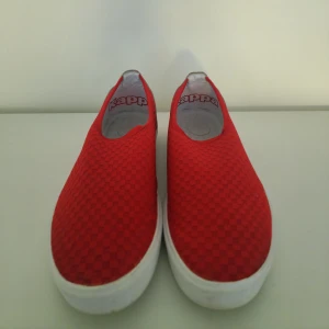 Röda slip-on sneakers från Kappa - Säljer ett par snygga röda slip-on sneakers från Kappa. Skorna har en cool textur på ovansidan och en vit sula. Baktill finns Kappas ikoniska logga i vitt. Perfekta för en avslappnad stil och enkla att ta på och av. Använda men i bra skick!