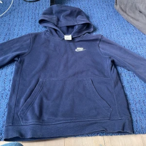 Mörkblå hoodie från Nike - Säljer en snygg och bekväm mörkblå hoodie från Nike. Den har en klassisk design med en känguruficka framtill och en broderad Nike-logga på bröstet. Perfekt för både vardag och träning.