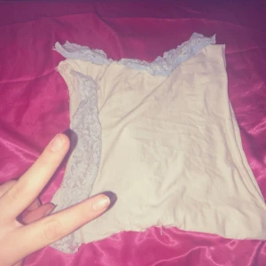 Vit topp med spetsdetaljer - Säljer en söt vit  topp med vackra spetsdetaljer längs axlarna. Toppen är ärmlös och har en romantisk känsla, perfekt för sommardagar eller en festlig kväll. Materialet känns mjukt och bekvämt mot huden.blå spets🎀🎀🎀