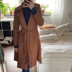 Trenchcoat i brun läderimitation från Helene Berman. Storlek 10 (38). Köpt second hand, använd en gång av förra ägaren, aldrig använd av mig. Mycket fint skick, ser ut som ny!