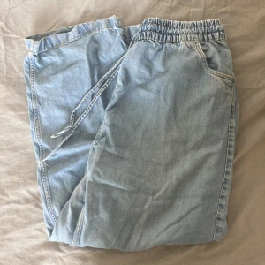 Ljusblå jeansbyxor med resårmidja - Säljer ett par ljusblå linnebyxor med resårmidja och snörning. De har en avslappnad passform och är perfekta för en casual look. Byxorna har både fram- och bakfickor, vilket gör dem praktiska och bekväma.