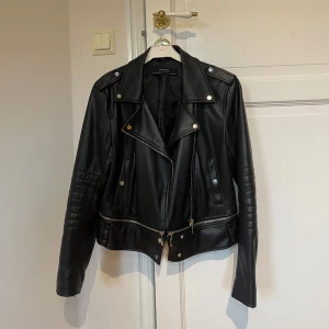Svart skinnjacka från Zara - Snygg svart skinnjacka från Zara i mycket bra skick. Den har en cool bikerstil med dragkedja och knappar. Jackan är långärmad och har quiltade detaljer på ärmarna. Perfekt för höst och vår!