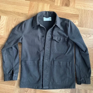 Grön/”Olive”overshirt jacka från A Day's March - Säljer en Patch Pocket Sturdy Twill Overshirt! en stilren ”olive” färgad overshirt från A Day's March i storlek S (ORIGINAL PRIS 1600kr).  Den har långa ärmar och knappar framtill samt en praktisk bröstficka med knapp. Perfekt under alla säsonger beroende på hur man klär upp den. Passar både till vardags och lite mer uppklädda tillfällen. 