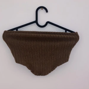 Brun stickad halsduk - Säljer en mysig brun stickad  perfekt för kyliga dagar. Den är mjuk och varm, idealisk för höst och vinter.  en enkel design som passar till det mesta. Perfekt för att hålla värmen och stilen på topp!