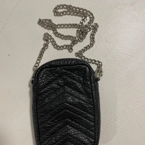 Svart axelväska från Sofie Schnoor - Snygg svart axelväska från Sofie Schnoor med kedjerem. Väskan har ett quiltat mönster på framsidan och en slät baksida. Perfekt för att bära med sig det viktigaste på stan eller till fest. Den är i mycket bra skick och passar till alla säsonger. 